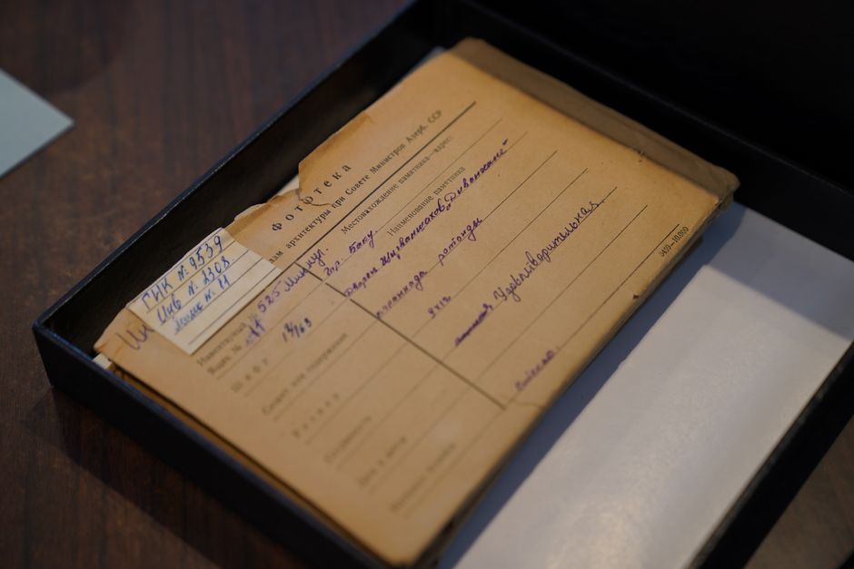 An old Russian document placed inside an archive box on a wooden desk.